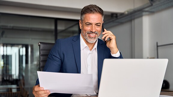 A business man looking at laptop as well talking on his cellphone